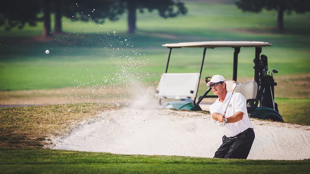 A golfer splashes a shot out of a greenside bunker